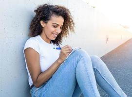 Hispanic female happily taking notes while sitting on the ground photo