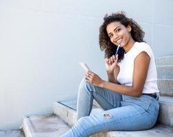 Hispanic female happily taking notes while sitting on the stairs photo