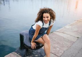 chica latina feliz sentada en un muelle foto