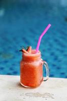 Glass of strawberry smoothie and fresh strawberries on top and have swimming pool background. Healthy food and drink concept.