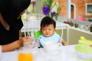 Mother feeding food to her son during breakfast at restaurant. Asian baby eating with mother. photo