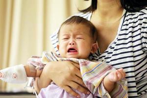 Asian baby crying in hospital with mother. Sick child with mother in hospital photo