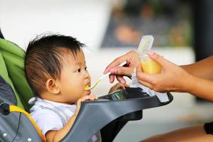 Mother hands feeding food for Asian baby on stroller. Boy eating. photo