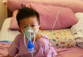niño asiático haciendo inhalación con un nebulizador en el hospital. niño enfermo. foto