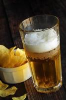 Light foamy beer with potato chips on a wooden table. photo