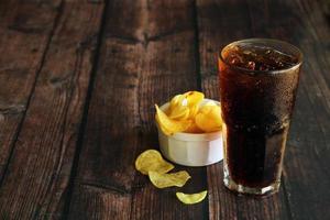 A glass of iced cola with potato chips on wooden table. Soft drinks and potato crisps. photo