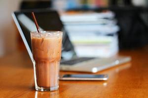 A glass of iced chocolate on wooden table with blurred smartphone and laptop  background. photo