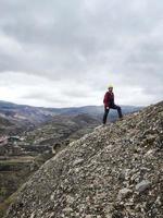 joven con casco de escalada amarillo mirando el paisaje montañoso foto