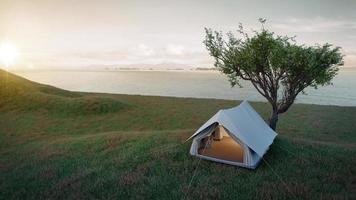 camping.evening scence.tent debajo del gran árbol en un prado, colina, montañas con fondo de mar. Representación 3d foto