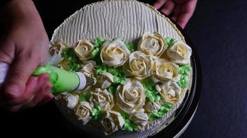 Köchin, die Rosen aus Sahne für die Dekoration von Kuchen herstellt, während sie hausgemachte Backwaren von oben auf schwarzem Hintergrund macht video