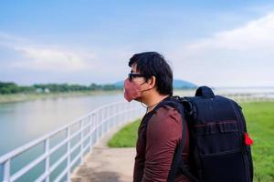 backpack Asian man wear fabric protective face mask during travel at dam lake photo