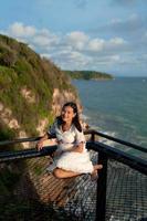 Asian woman tourist sit at net terrace on top hill with view above cliffs and sea in evening with sunlight, sky view photo