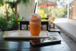 Thai milk tea frappe in takeaway cup served with wooden tray  near mobile phone photo