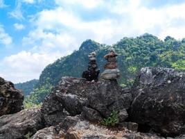 apilando piedras o guijarros en una gran roca áspera con vistas a la montaña verde y un cielo azul brillante nublado en el fondo. naturaleza pacífica y tranquila. piedra mía. foto