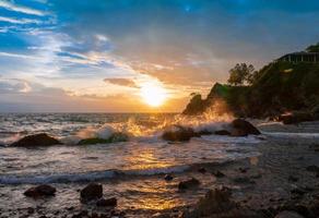 splash sea waves on rock beach with sunset rain clouds sky with light flare photo