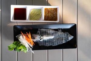 fresh raw sliced squid on dish on white wooden table photo