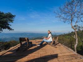 Asian woman sit and relax at wooden balcony with mountain view with blue sky at Doi Chang, travel attraction in Chiang Rai, Thailand photo