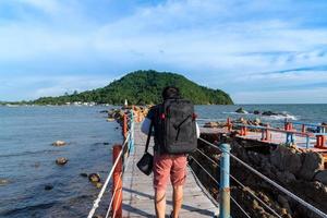 Asian man tourist backpaker walking on wooden bridge with rope rail bridge to viewpoint to see white pagoda on the stone in the middle of the see photo