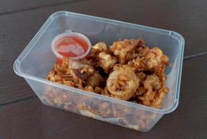 deep crispy fried sliced squid with garlic served in take away container with chili sauce on wooden table photo