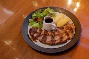 sliced grilled pork steak with barbecue pepper sauce side with salad and mashed potatoes on wooden dinner table photo