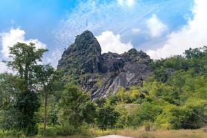 old mining rock mountain with fresh green forest and cloudy bright blue sky in Thong Pha Phum, Kanchanaburi, Thailand. limestone hill. adventure nature travel. photo