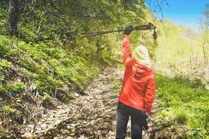 Back view determined hiker solo woman lift up nordic stick out of joy on hike up outdoors in nature. photo