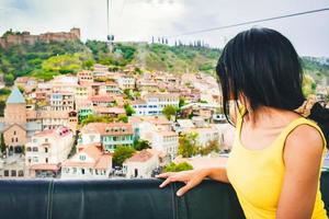 joven turista caucásica mira a través de la ventana al casco antiguo en teleférico, tbilisi, georgia foto