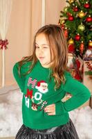 hermosa niña en suéter verde frente al árbol de navidad foto