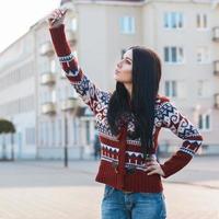 Beautiful girl doing Selfie on phone in city. photo