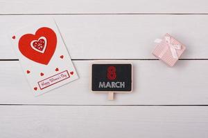 Blackboard with 8 march tag, a gift and a card with red hearts on a white table. photo