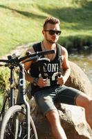 Stylish young man with a bike sitting on a rock. Black T-shirt with print 23 photo