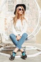 Beautiful fashionable girl sitting in a white suspended chair.