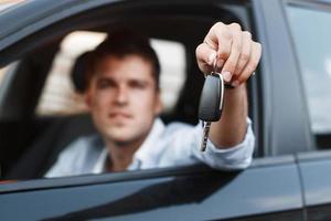 hombre de negocios sentado en un auto y dando una llave de auto. foto