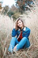 Beautiful positive girl in denim clothes sitting in autumn grass. photo