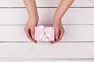 Girl gives a gift. Female hand holding a gift with a bow above the table. photo