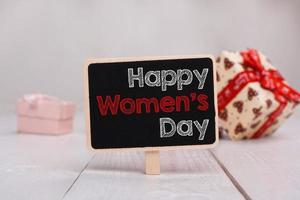 mensaje del día de la mujer feliz escrito en una pequeña pizarra. fondo con regalos. foto