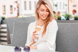 Beautiful girl sitting in a summer cafe and eating ice cream in a waffle cone. Woman hand holding waffle with ice cream. photo