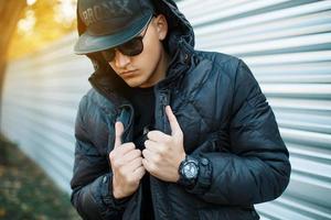 Portrait of beautiful fashionable guy in a stylish black dress. The hood on his head. Beautiful sunny autumn day photo