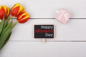 Blackboard with Happy Women's Day, bouquet of tulips and a gift with a bow on the table. photo