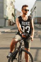joven hipster con bicicleta sentada en una bicicleta en la ciudad. camiseta negra con estampado 23 foto