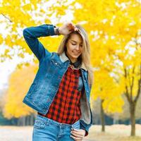 mujer joven en ropa de mezclilla con hojas de otoño en la mano y fondo de jardín de arce amarillo de otoño foto