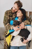 una pareja ucraniana, un soldado con uniforme militar y una niña envuelta en una bandera ucraniana sostienen un perro en sus brazos, felices juntos. foto