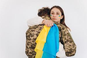 A Ukrainian girl hugs and holds a yellow and blue flag of a military man in uniform and says goodbye to him. photo