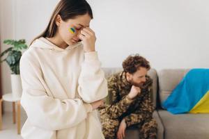 una mujer ucraniana llora y se despide de su esposo militar con un uniforme que sostiene una bandera ucraniana en casa foto