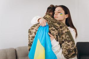 A Ukrainian girl hugs and holds a yellow and blue flag of a military man in uniform and says goodbye to him. photo