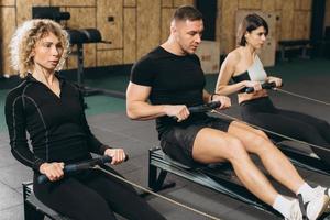 Young man and beautiful women working out with rowing machine at crossfit gym. photo