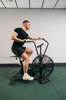 hombre fuerte que usa bicicleta de aire para hacer ejercicio cardiovascular en el gimnasio de entrenamiento cruzado. foto