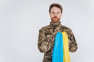 Ukrainian patriot soldier in military uniform holds a hand on a heart with a yellow and blue flag on a white background photo