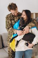 A Ukrainian couple, a soldier in military uniform and a girl wrapped in a Ukrainian flag hold a dog in their arms, happy together. photo