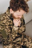 Portrait of emotional young bearded Ukrainian patriot soldier in military uniform sitting on the office sofa photo